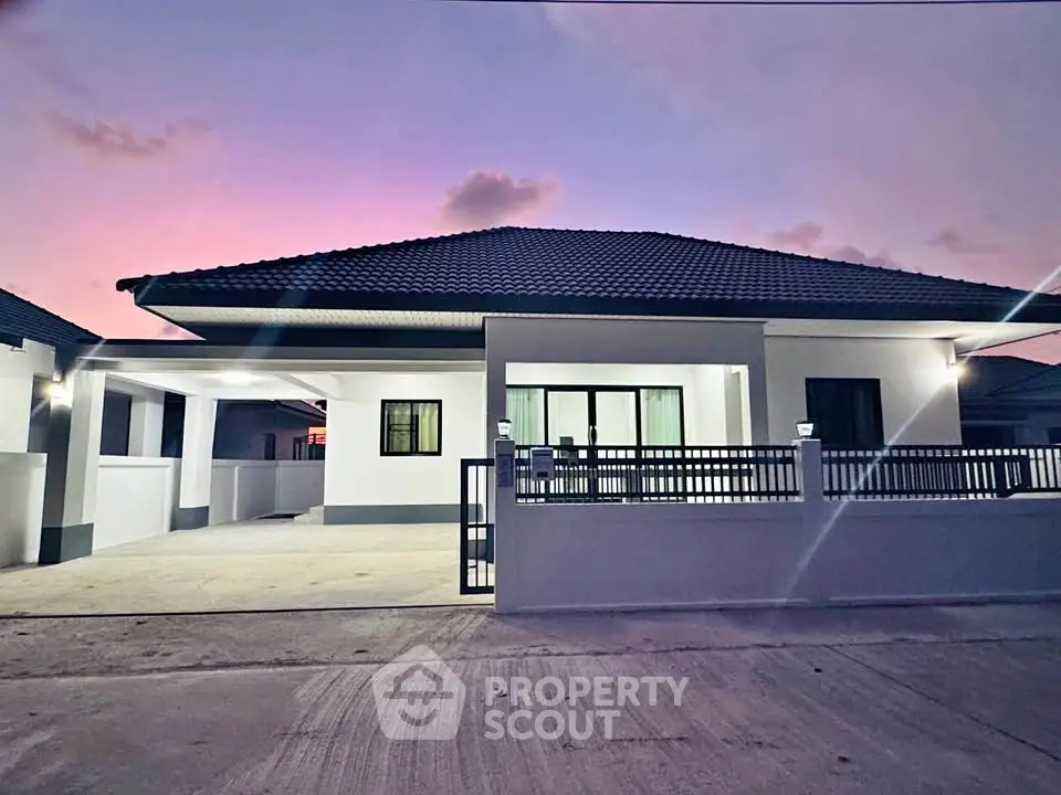 Modern single-story house with sleek design and spacious driveway at sunset.