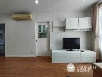 Spacious and well-lit living room with polished hardwood floors, modern white storage units, and a sleek wall-mounted TV setup, perfect for comfortable urban living.