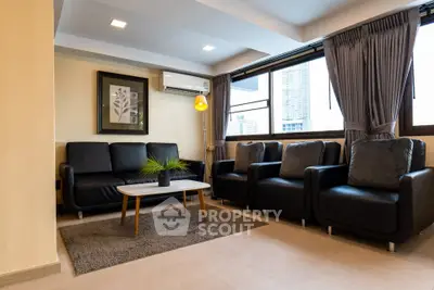 Modern living room with sleek black furniture and large windows offering city views.