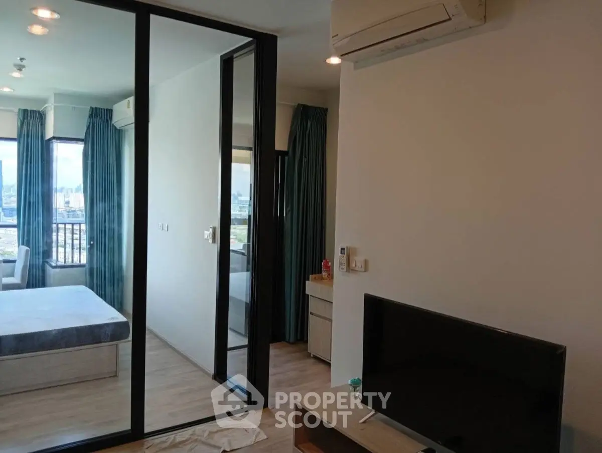 Modern apartment interior with bedroom and living area, featuring large windows and air conditioning.