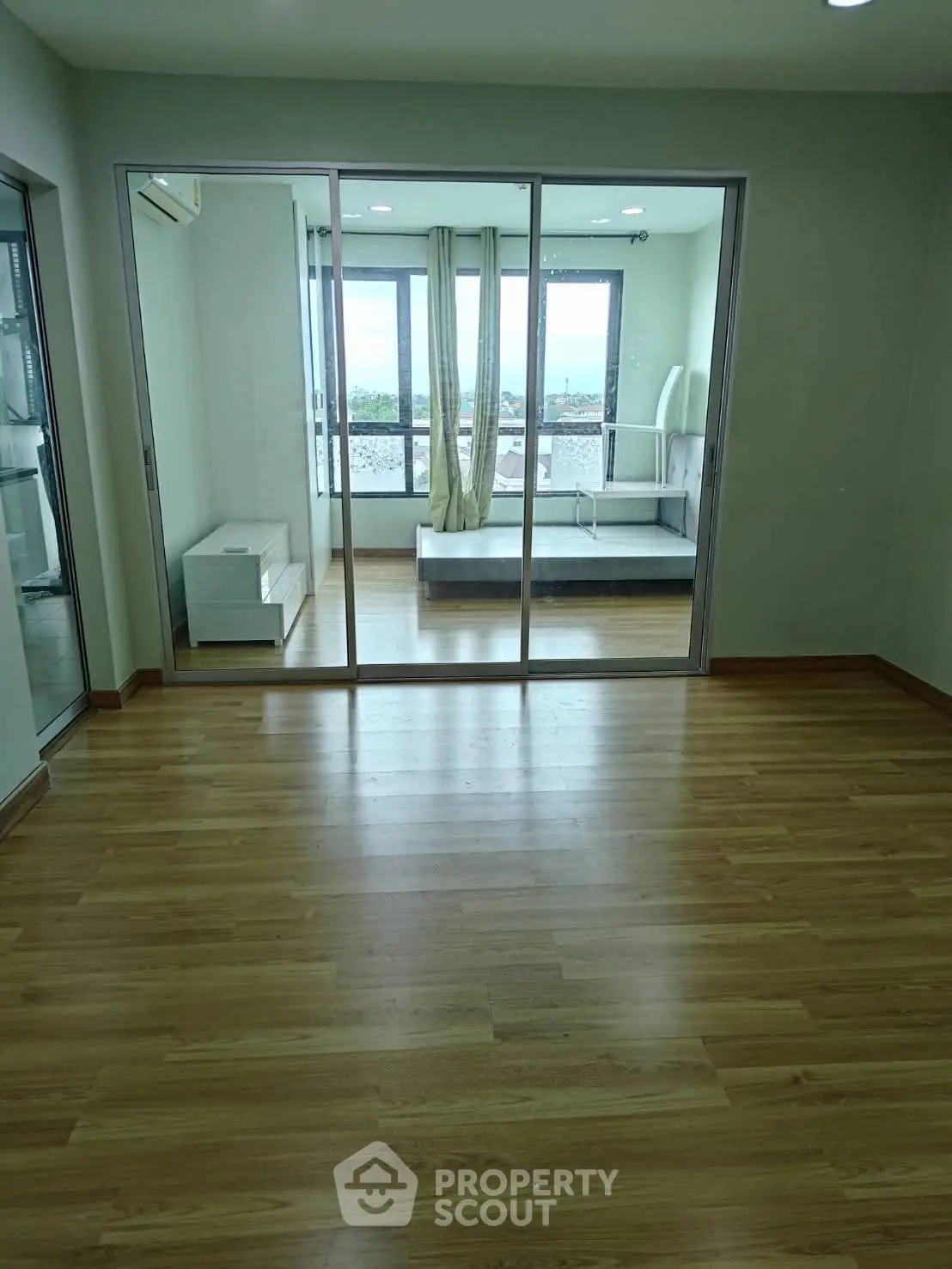 Spacious bedroom with wooden flooring and large windows offering natural light and city views.