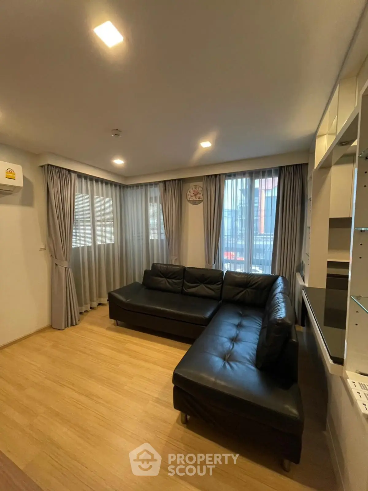 Modern living room with black leather sectional sofa and large windows with curtains.