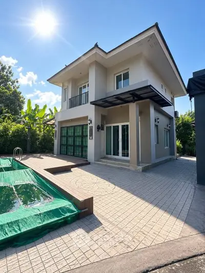 Stunning modern two-story house with pool and lush greenery under a bright blue sky.
