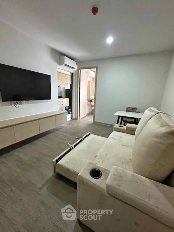 Modern living room with plush sofa, wall-mounted TV, and sleek wooden flooring in a cozy apartment.
