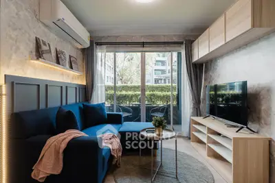 Modern living room with stylish decor and large window overlooking greenery, featuring a cozy blue sofa and sleek TV setup.