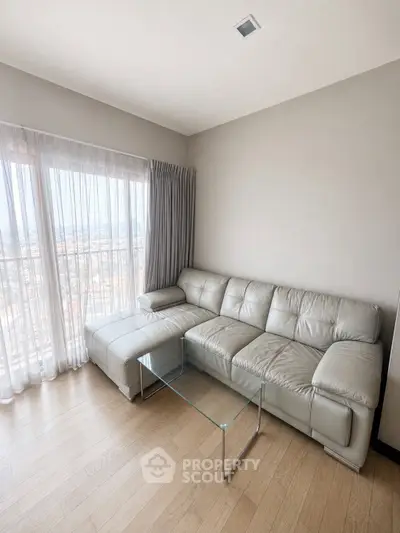 Modern living room with leather sofa and glass coffee table, featuring large windows with city view.