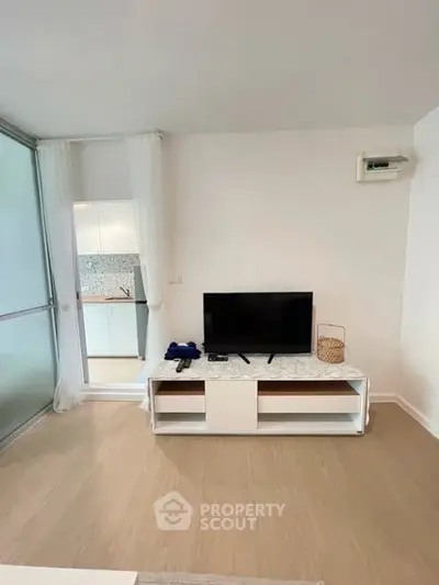 Modern living room with TV and sleek furniture, open view to kitchen area.