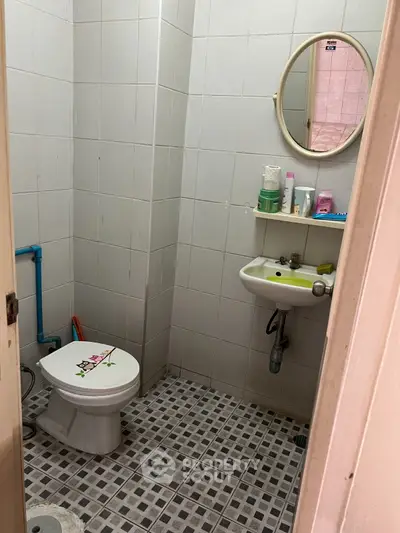 Compact bathroom with tiled walls and floor, featuring a round mirror and essential toiletries.