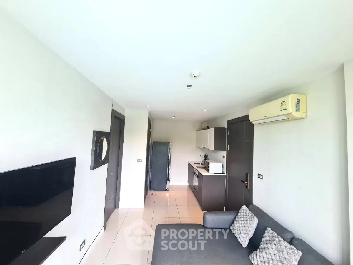 Modern living room with open kitchen, sleek furniture, and air conditioning in a bright apartment.