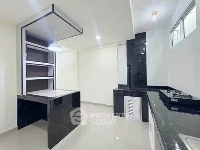 Modern kitchen with sleek black marble countertops and gas stove, featuring open layout and stylish lighting.