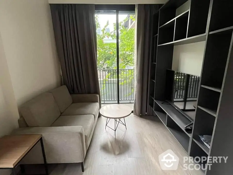 Modern living room with sleek furniture and balcony access, featuring large windows for ample natural light and a serene view.