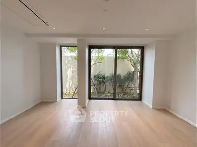 Spacious living room with large windows and garden view, featuring elegant wooden flooring.