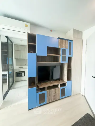 Modern living room with stylish blue and wood entertainment center and sleek kitchen view.