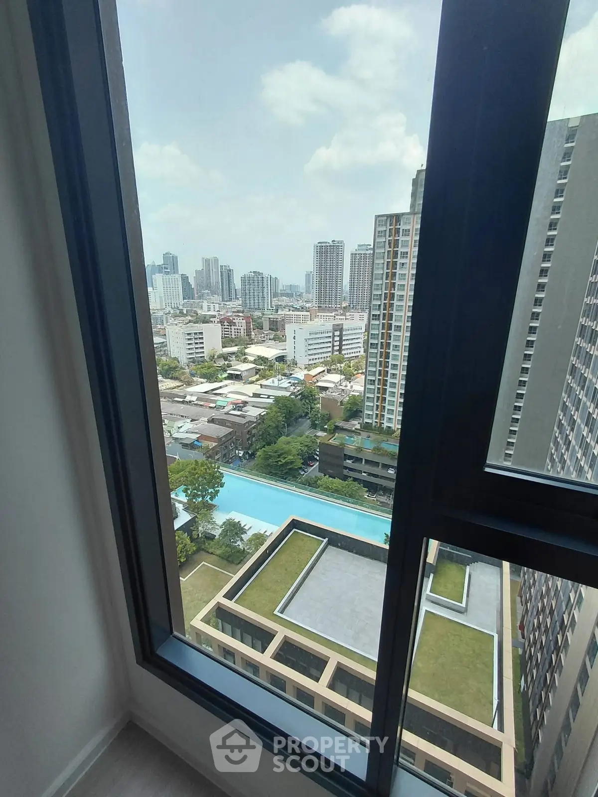 Stunning high-rise view from apartment window overlooking cityscape and pool area.