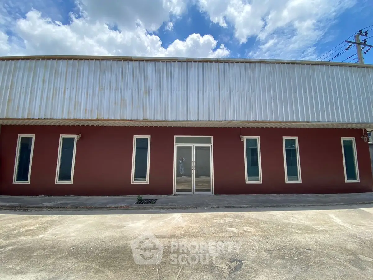 Industrial warehouse exterior with metal facade and large entry doors under a bright blue sky.