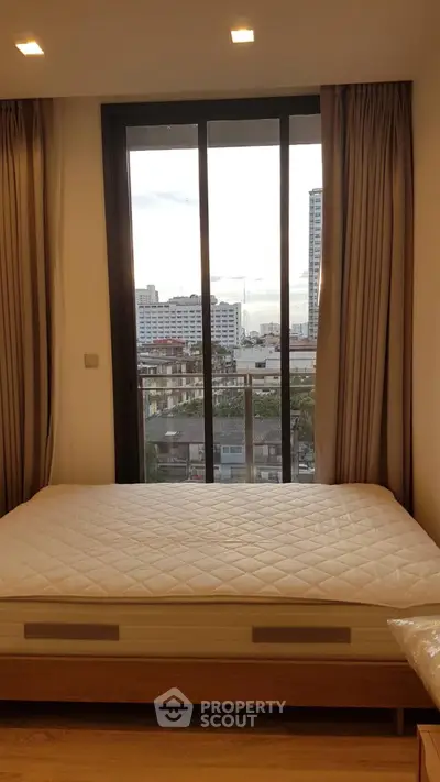 Modern bedroom with city view and large window, featuring a comfortable bed and elegant curtains.
