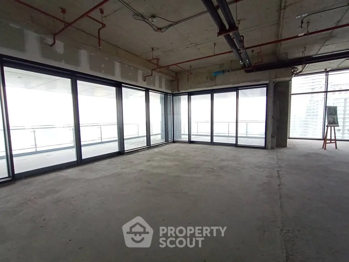 Spacious unfinished apartment with large windows and balcony offering potential for customization.