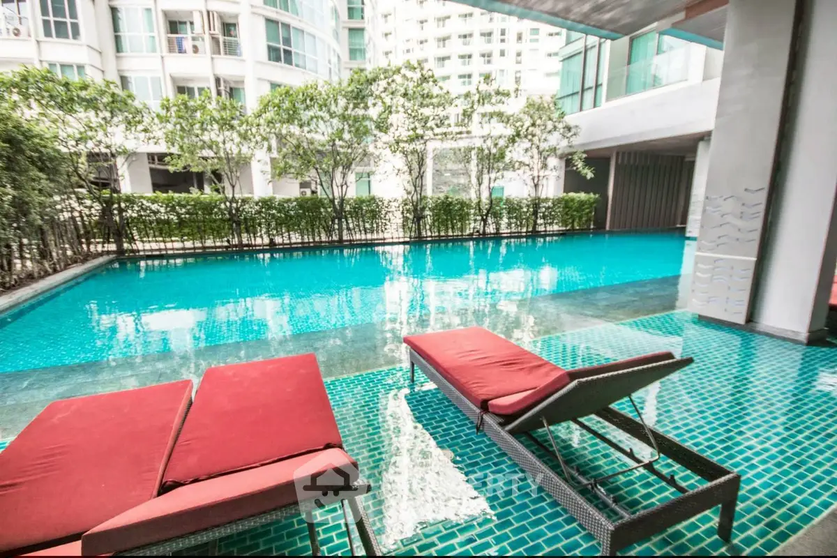 Luxurious condominium pool area with modern lounge chairs and lush greenery, perfect for relaxation and leisure.