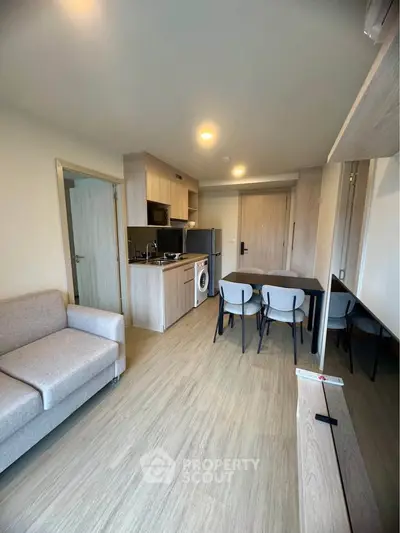 Modern open-plan living room with kitchen and dining area, featuring light wood finishes and cozy furniture.