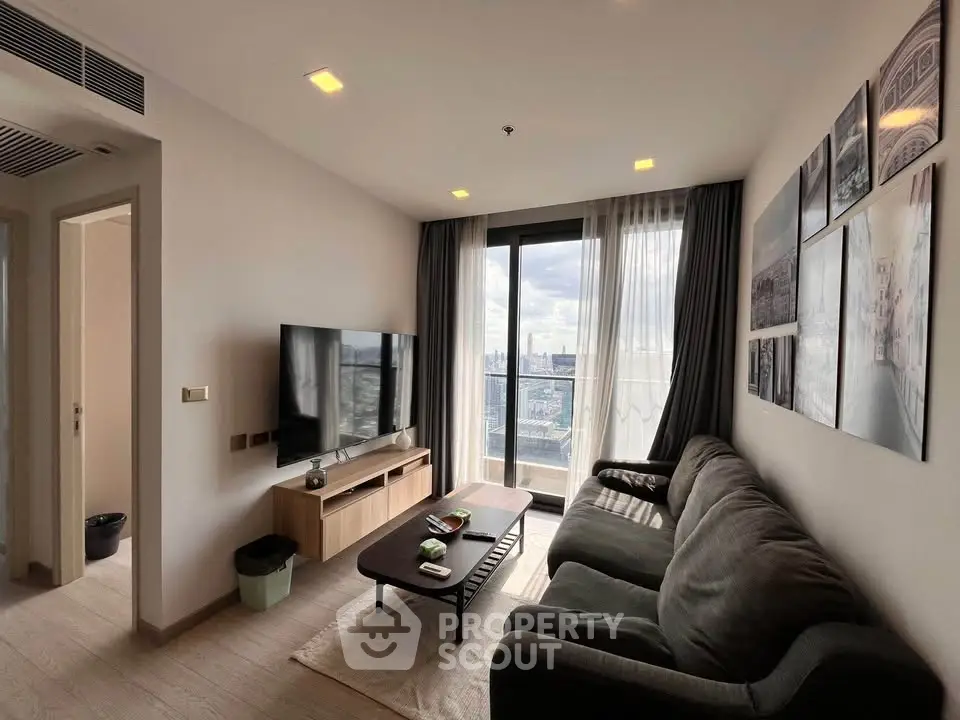 Modern living room with city view, featuring a cozy sofa, wall art, and a large TV, leading to a balcony.