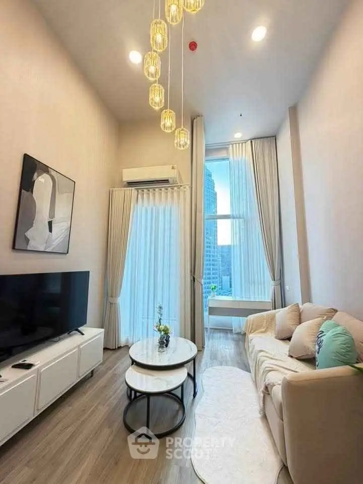 Modern living room with high ceiling, elegant chandelier, and large window offering city view.