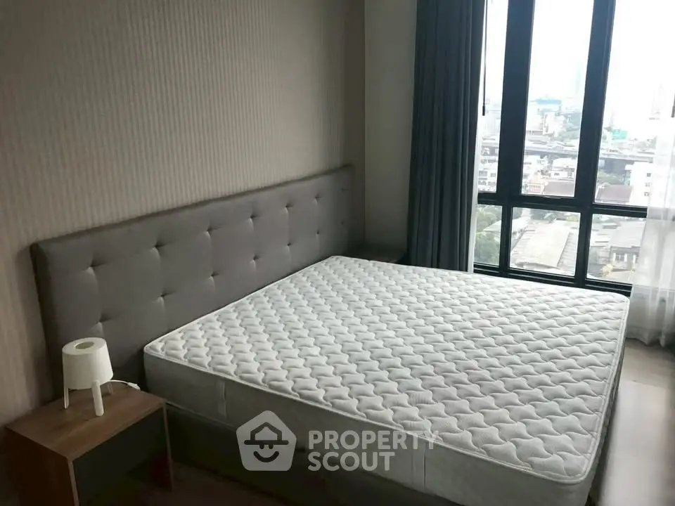 Spacious bedroom with large window offering city views, featuring a comfortable bed and modern decor.