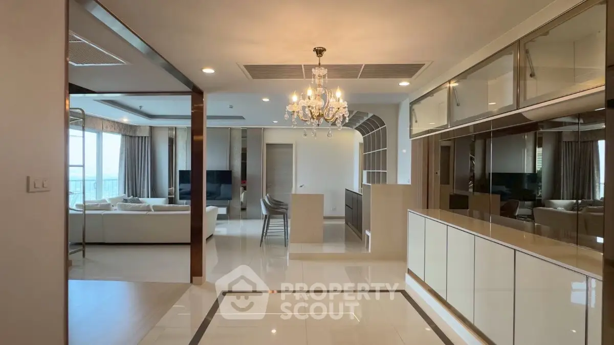 Luxurious open-plan living room with chandelier and modern kitchen, featuring elegant decor and spacious design.