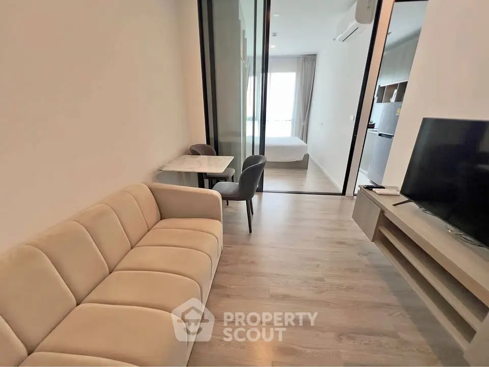 Modern living room with sleek furniture and open layout leading to a cozy bedroom.