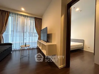 Modern living room with sleek TV setup and view into cozy bedroom, featuring elegant curtains and wooden flooring.