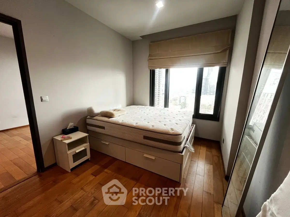 Cozy bedroom with wooden flooring and large window offering city view