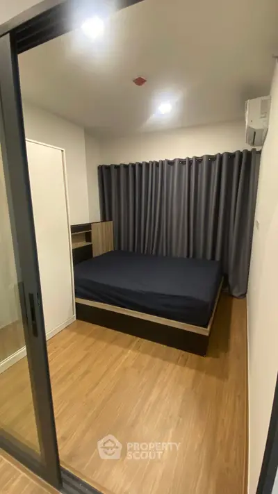 Modern bedroom with wooden flooring and dark curtains in a cozy apartment.