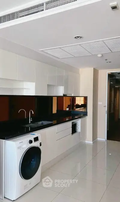 Modern kitchen with sleek cabinetry and built-in appliances, featuring a washing machine and glossy black countertops.