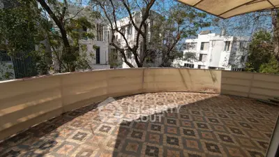 Spacious balcony with tiled flooring and scenic view of surrounding trees and buildings.