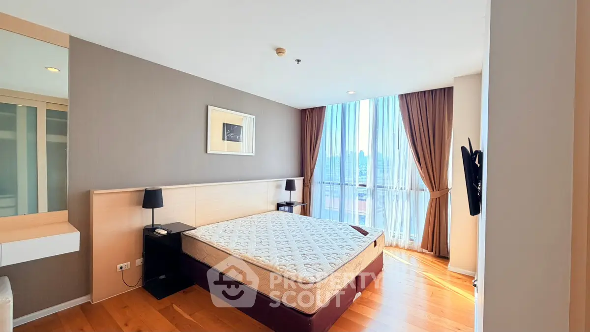 Spacious bedroom with large window and wooden flooring in modern apartment.