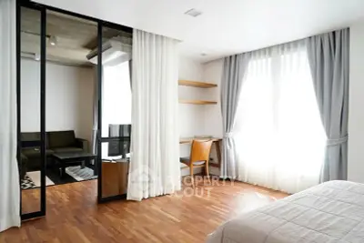 Modern bedroom with wooden flooring and sliding glass doors leading to a cozy living area.
