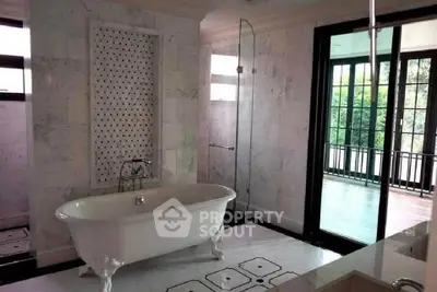 Luxurious bathroom with elegant freestanding bathtub and glass shower, overlooking a serene balcony view.