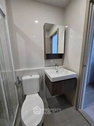 Modern bathroom with sleek fixtures and minimalist design, featuring a wall-mounted sink and glass shower enclosure.