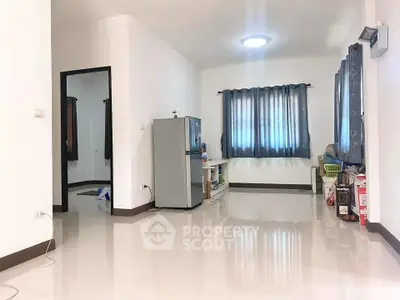 Spacious living room with glossy floor and natural light, featuring a refrigerator and modern decor.