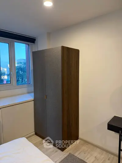 Cozy bedroom with modern wardrobe and large window offering natural light.
