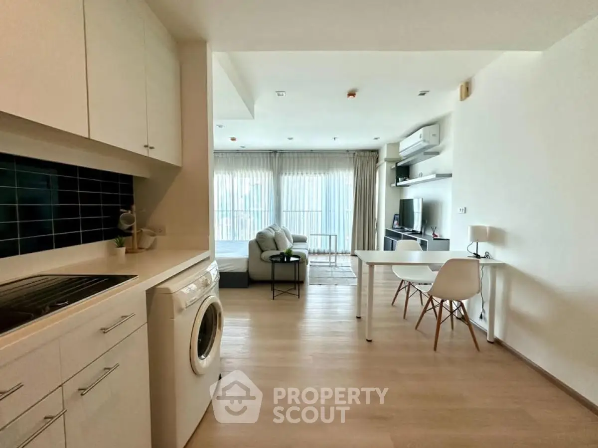 Modern open-plan living room with kitchen and washing machine, bright and airy space.