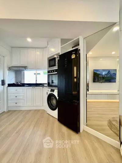 Modern kitchen with sleek appliances and open layout, featuring a washing machine and black fridge.