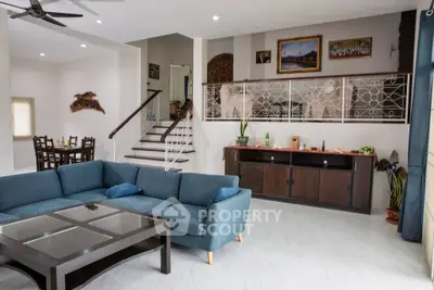 Spacious living room with modern decor and open dining area, featuring elegant staircase and stylish furniture.