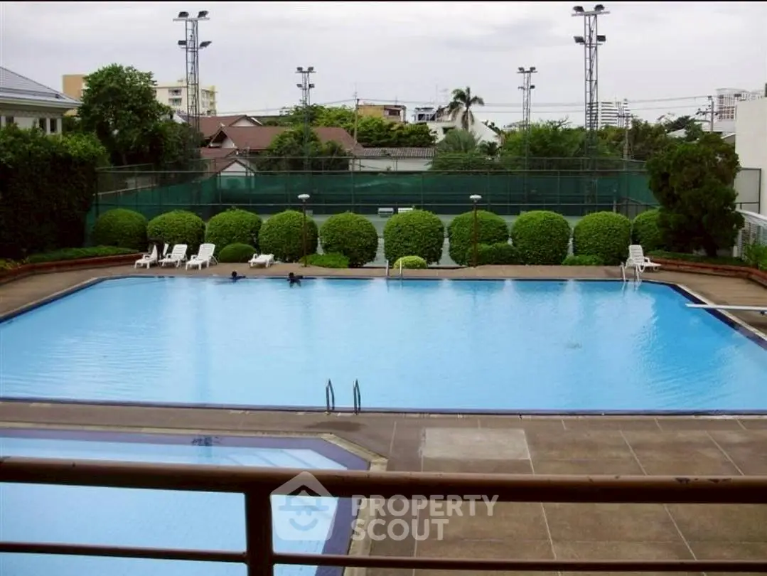 Luxurious outdoor pool with lush greenery and tennis courts, perfect for relaxation and recreation.
