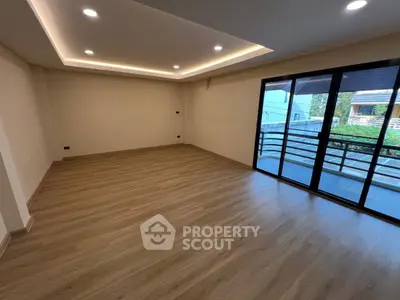 Spacious empty living room with wooden flooring and large balcony access.