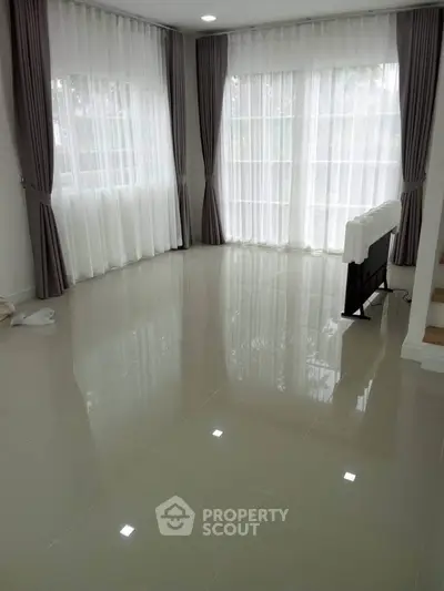 Spacious empty living room with large windows and glossy tiled floors, perfect for natural light lovers.