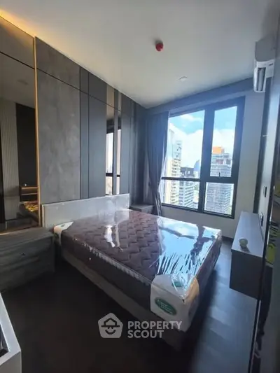 Modern bedroom with large windows offering city views, featuring a stylish bed and sleek decor.