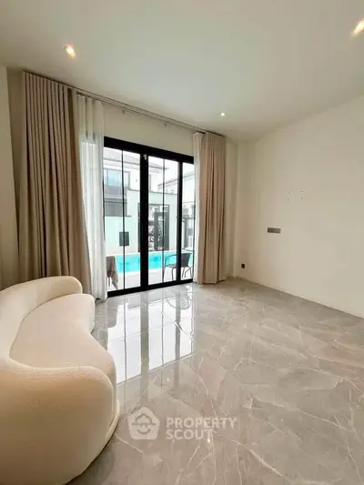 Spacious living room with elegant sofa and pool view through large glass doors.
