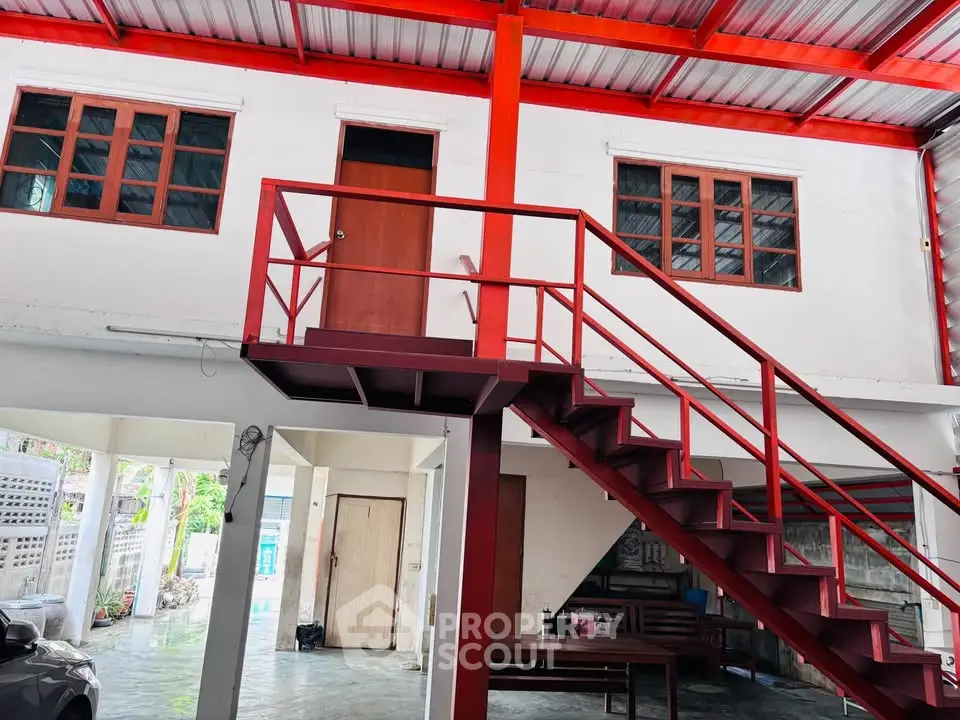 Spacious industrial-style loft with red metal staircase and large windows, perfect for creative workspace.