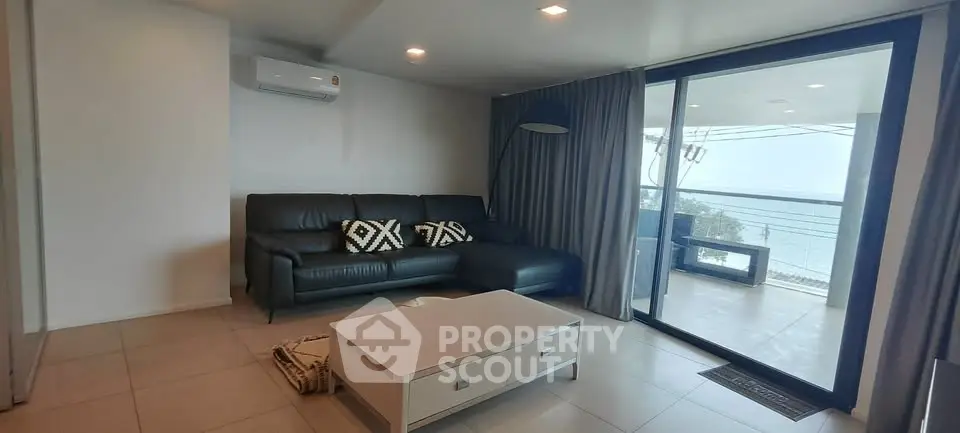 Modern living room with ocean view and balcony access, featuring sleek black sofa and stylish decor.