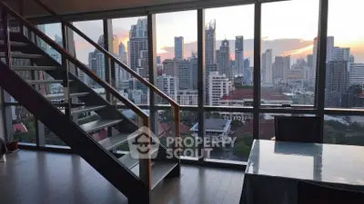 Stunning city view from modern apartment with floor-to-ceiling windows and sleek staircase.